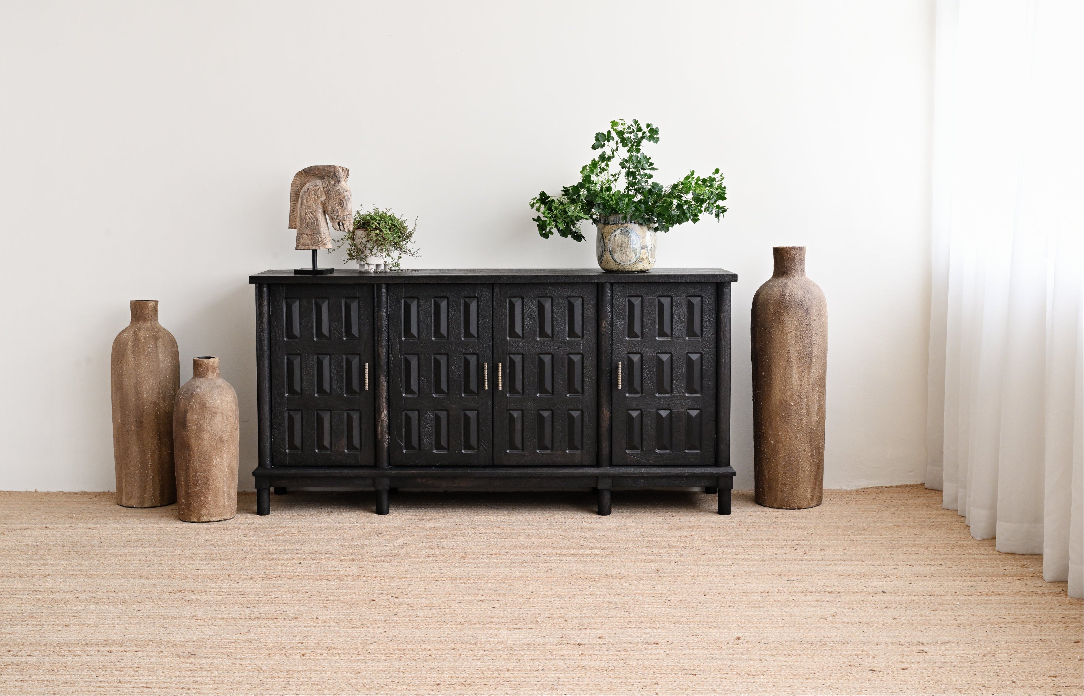 Black wooden sideboard with decorative vases and plants in a minimalistic room.