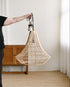 Person holding a wicker pendant light in a room with wooden furniture and white walls.
