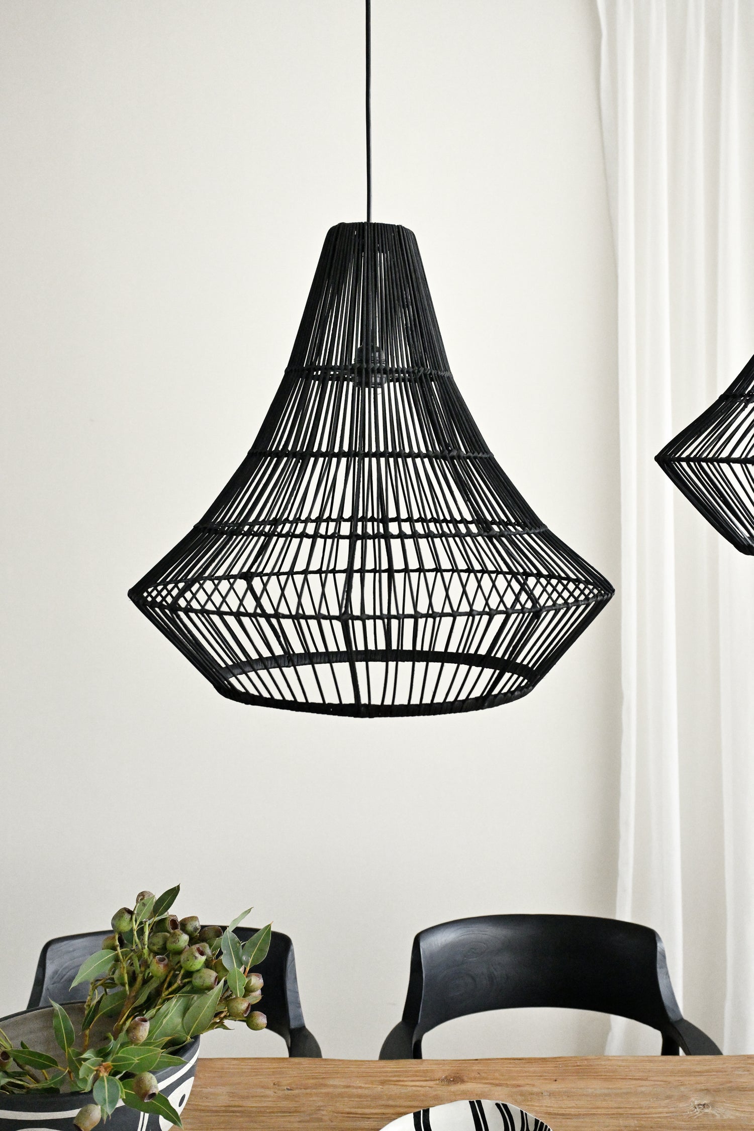 Black woven pendant light fixture hanging above a dining table with chairs.