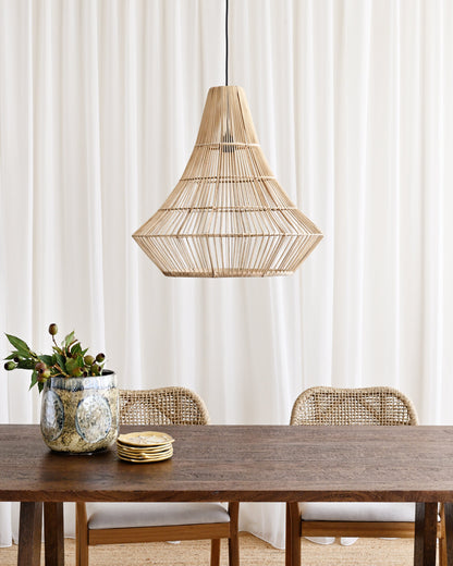 Dining area with a wooden table, chairs, and a wicker pendant light against a white curtain background.