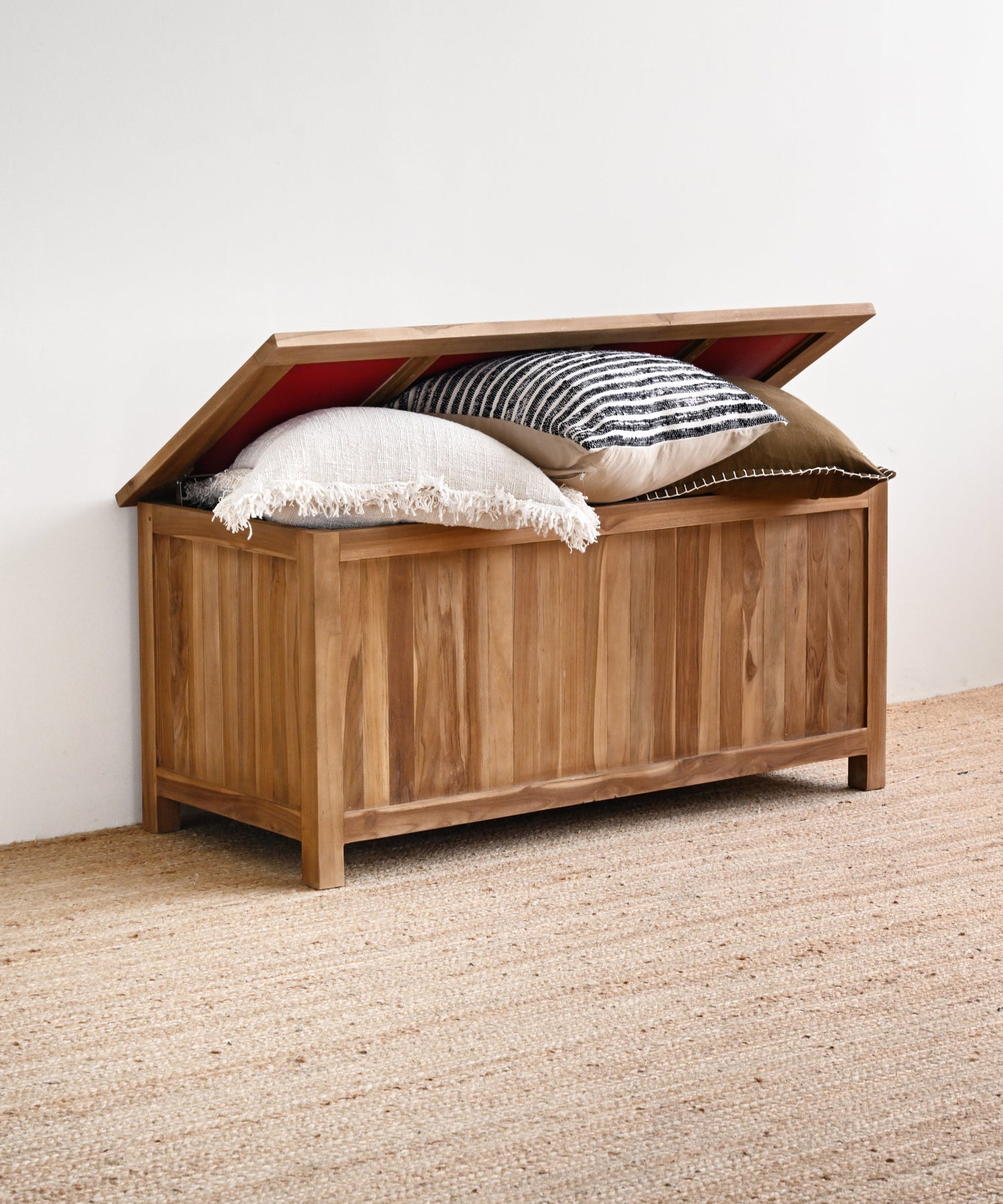 Wooden storage chest with pillows on a carpeted floor against a white wall