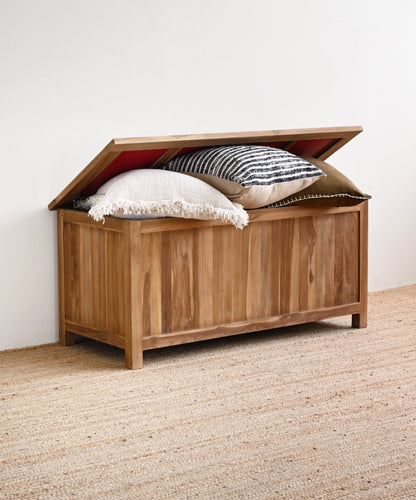 Wooden storage chest with pillows on a carpeted floor against a white wall