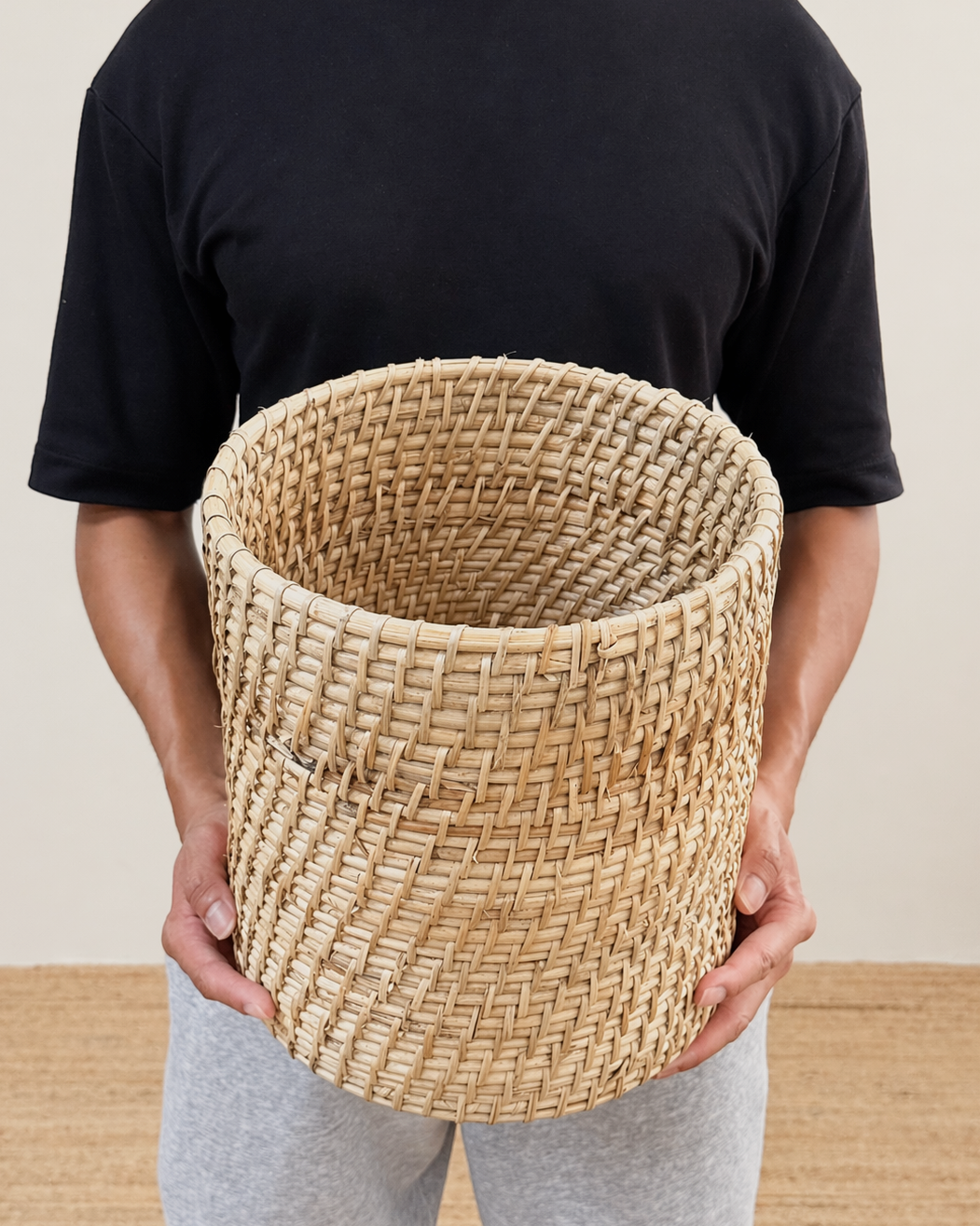 Person holding a woven basket against a neutral background
