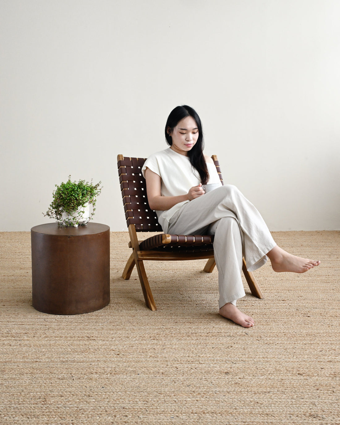 Woman sitting on a chair in a room with a textured floor and a small table with a plant.