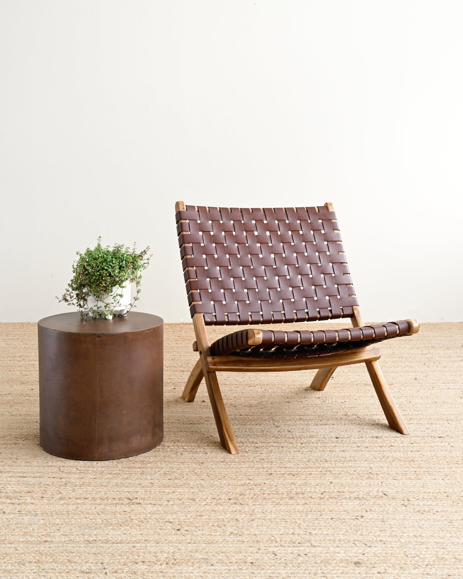 Brown woven chair and round wooden table on a light wood floor with a white wall background