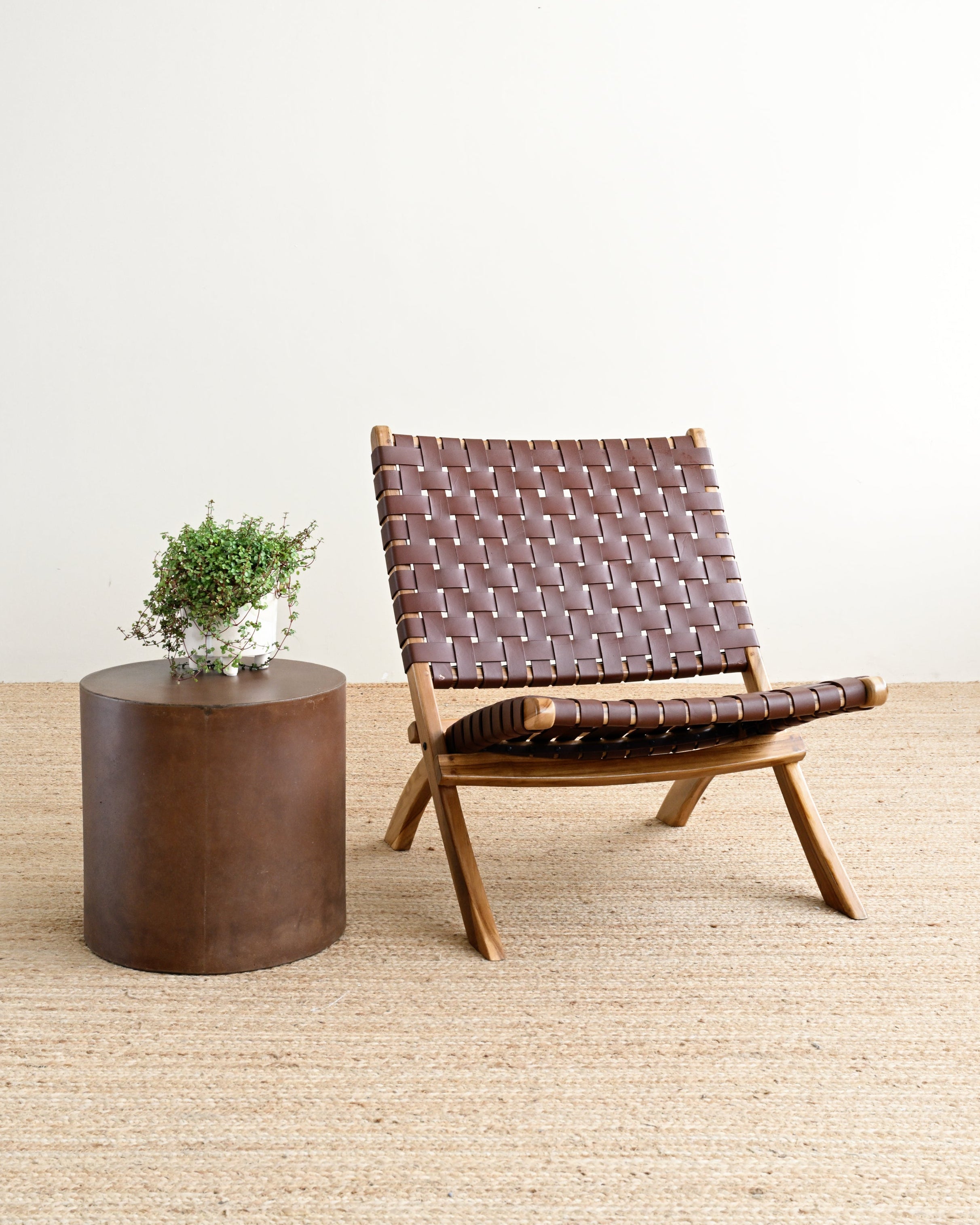 Brown woven chair and round wooden table on a light wood floor with a white wall background
