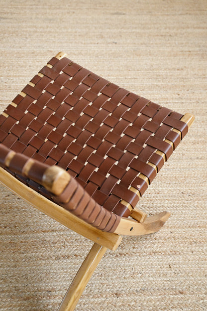 Brown woven stool with wooden legs on a beige textured background