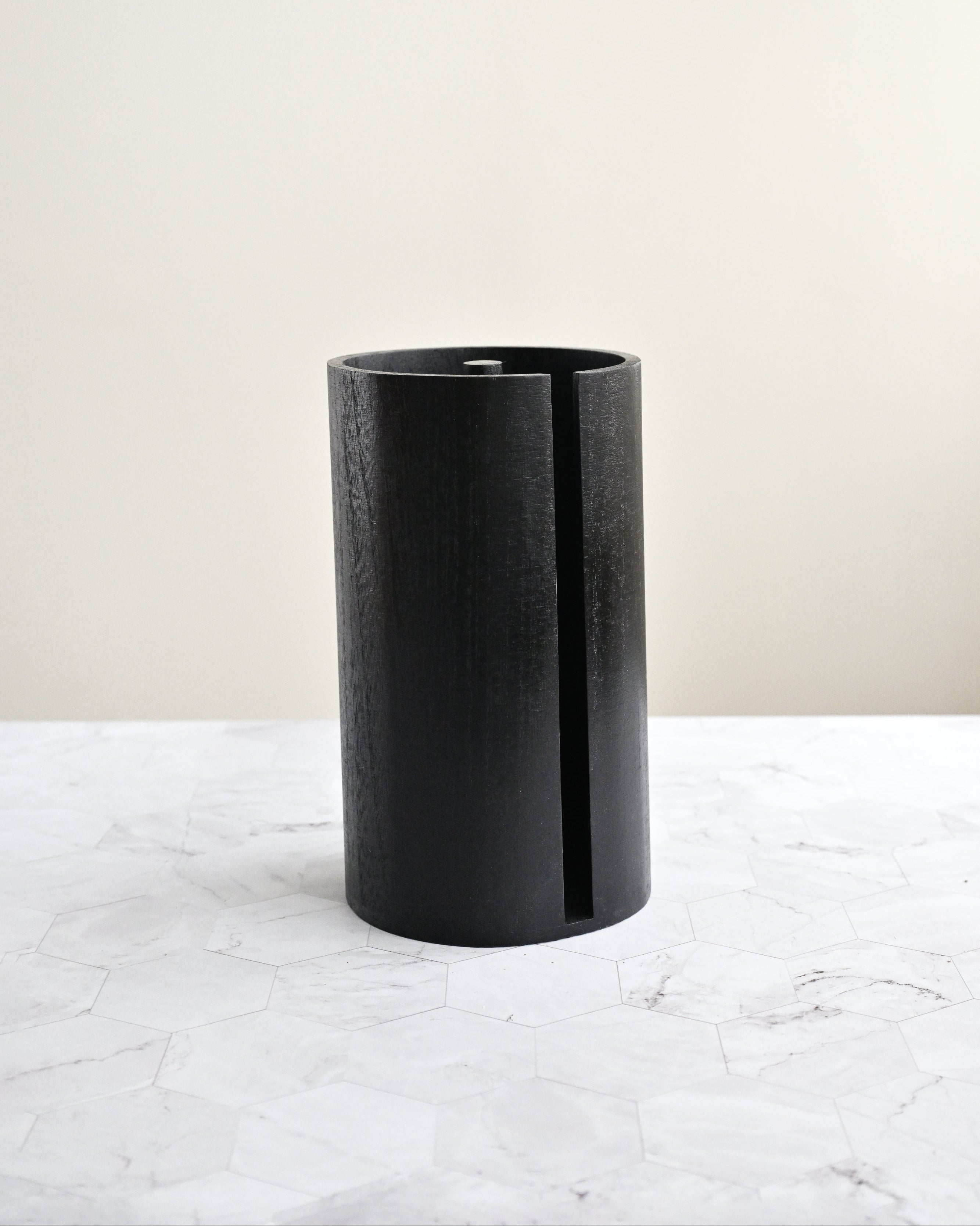 Black cylindrical vase on a white marble surface with a light beige background