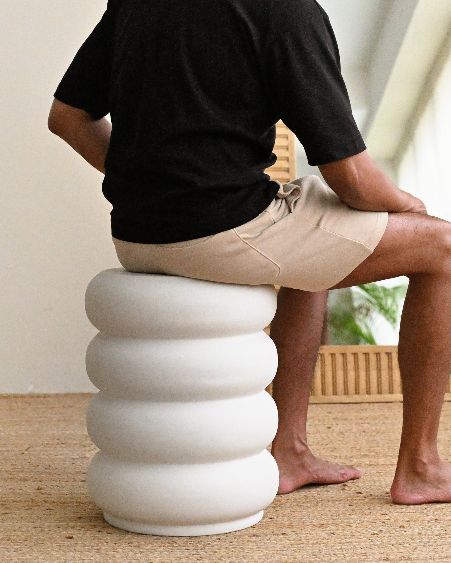 Person sitting on a white, ribbed stool in a room with a mirror and beige walls.