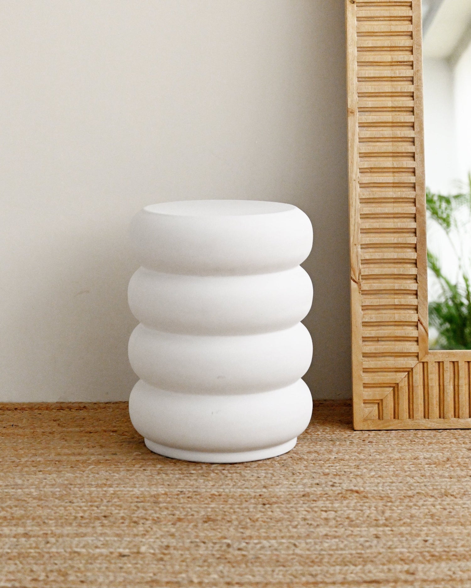 White concrete stool with stacked rings on a wooden floor next to a mirror.