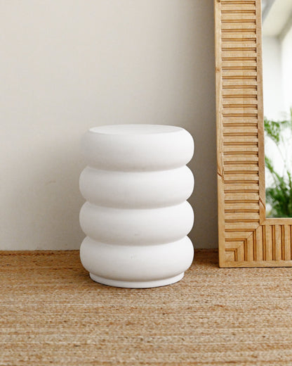 White concrete stool with stacked rings on a wooden floor next to a mirror.