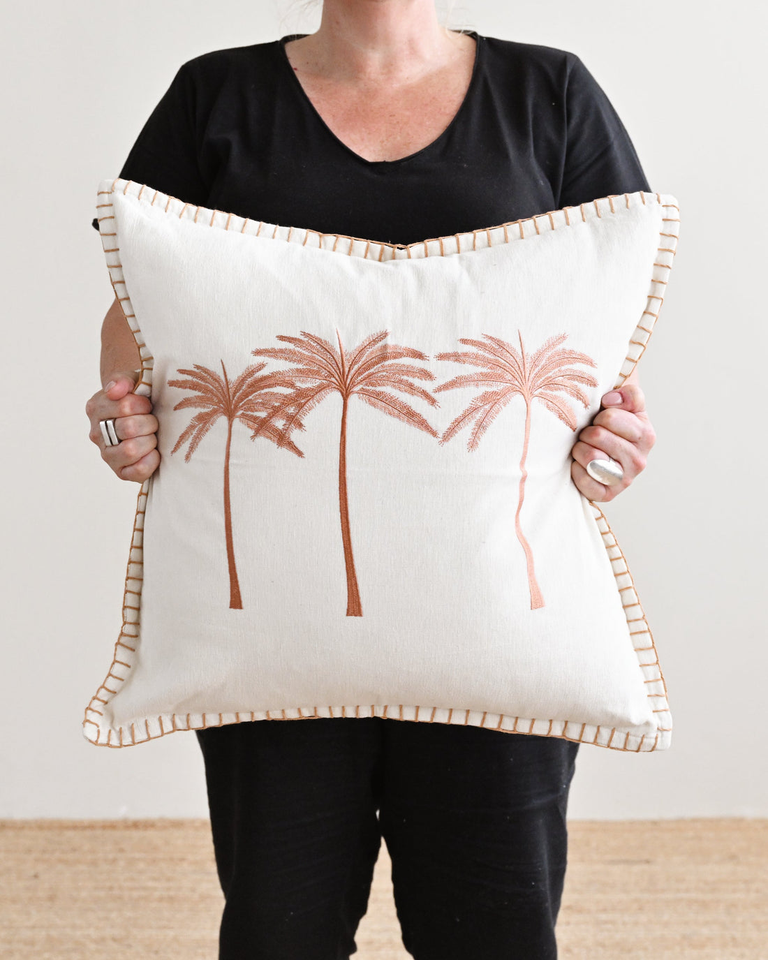 Person holding a decorative pillow with palm tree design against a plain background