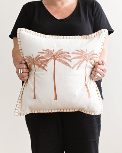 Person holding a decorative pillow with palm tree design against a plain background