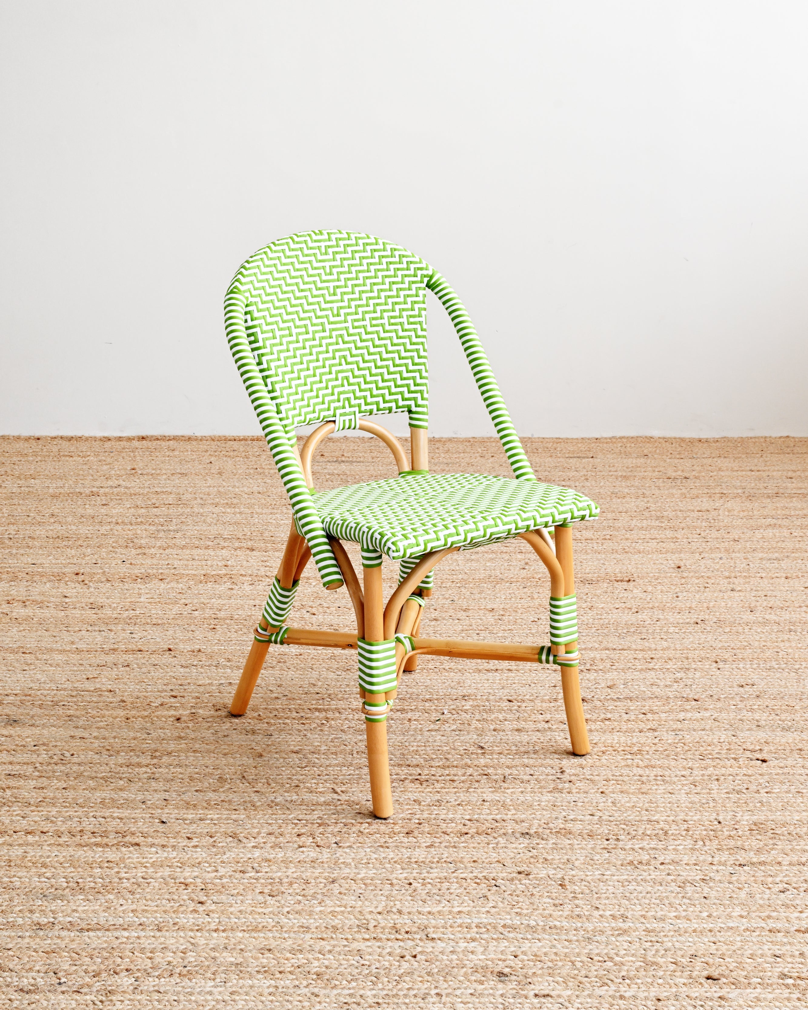 Green woven chair on a wooden floor with a white wall background