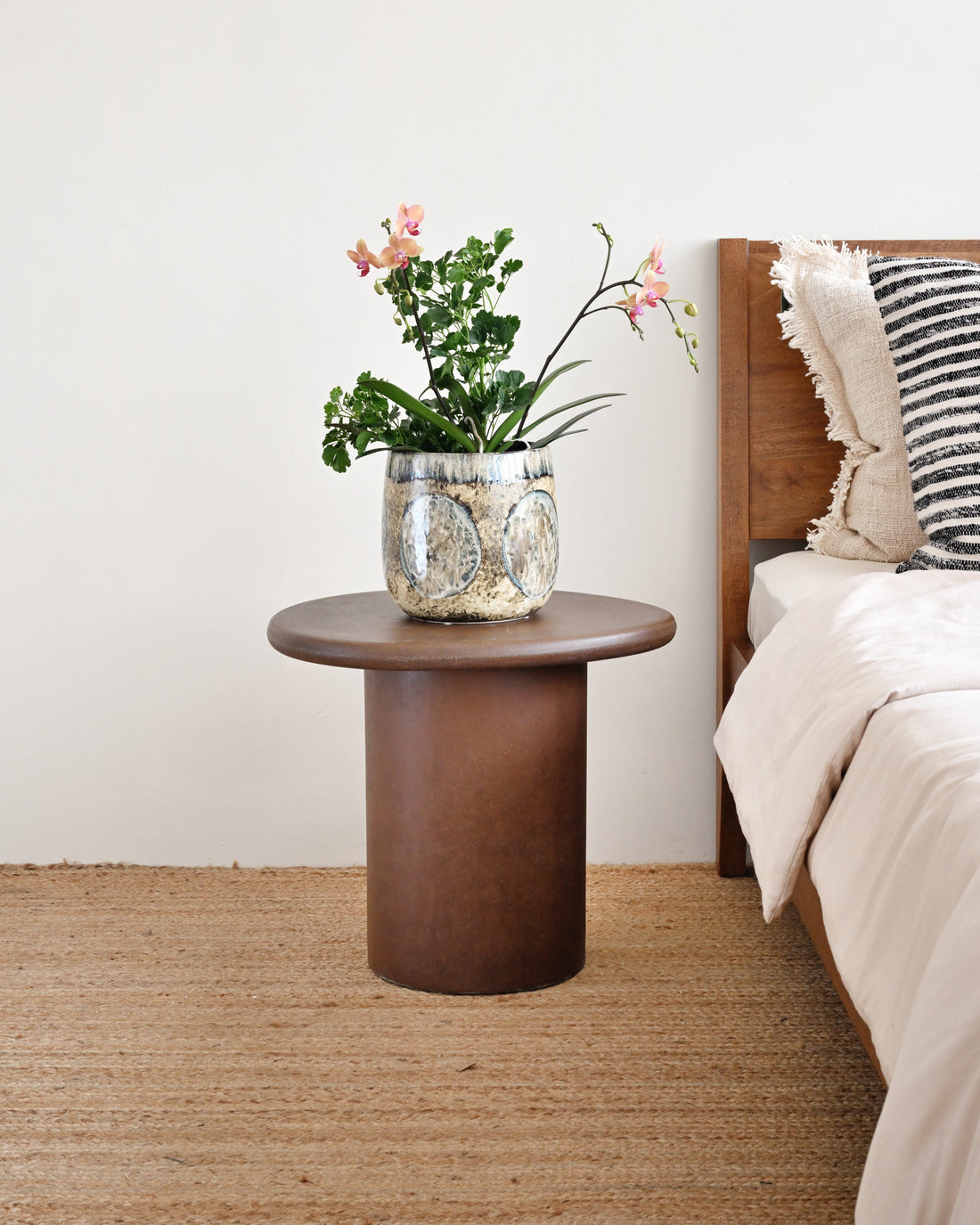 Wooden side table with a plant next to a bed with striped bedding.