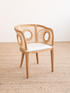Wicker chair with a white cushion on a textured beige floor.