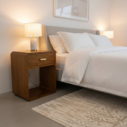 Wooden side table with a drawer and gold handle on a plain background