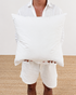 Person holding two white pillows against a neutral background