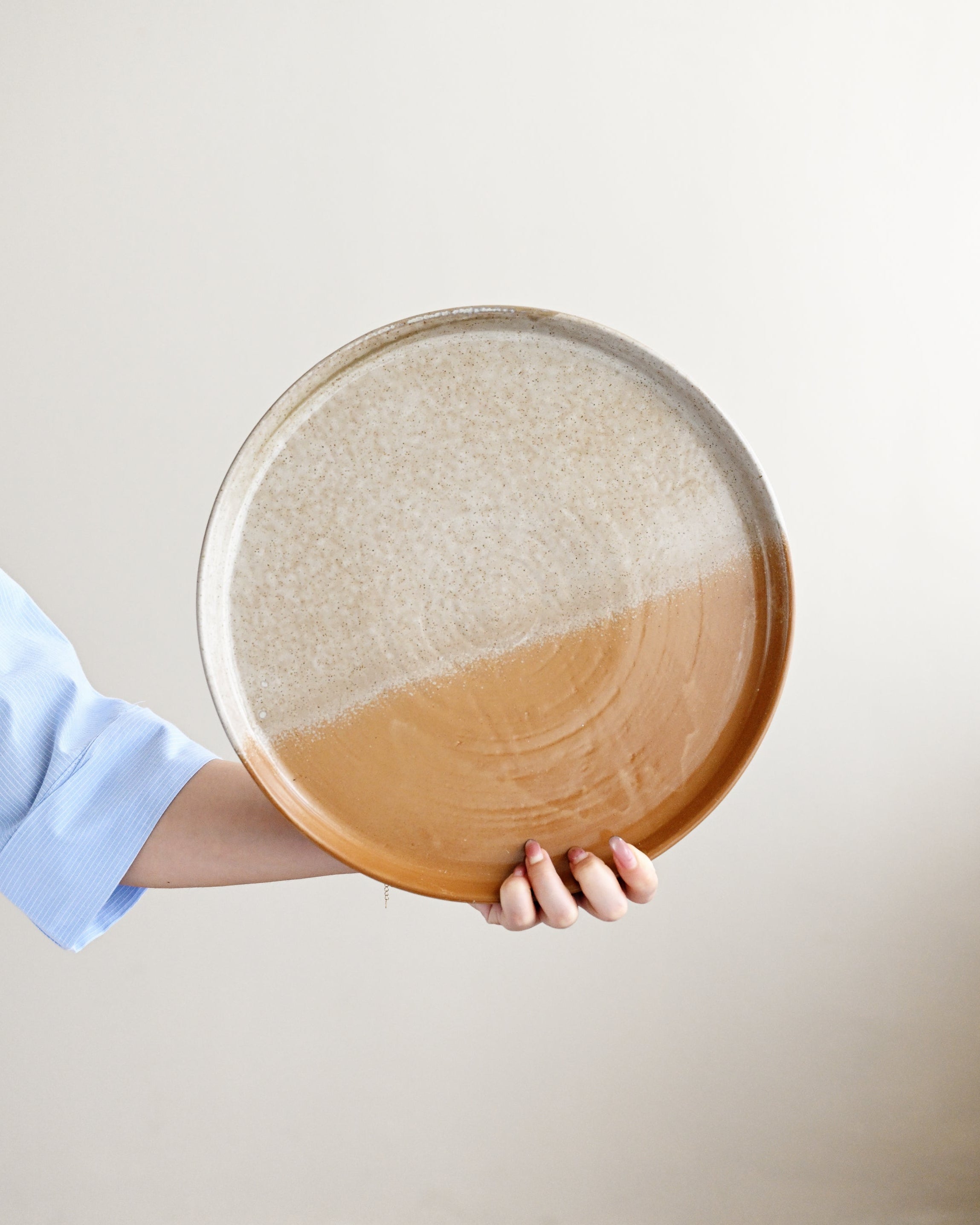 Person holding a round wooden tray with a gradient design against a plain background