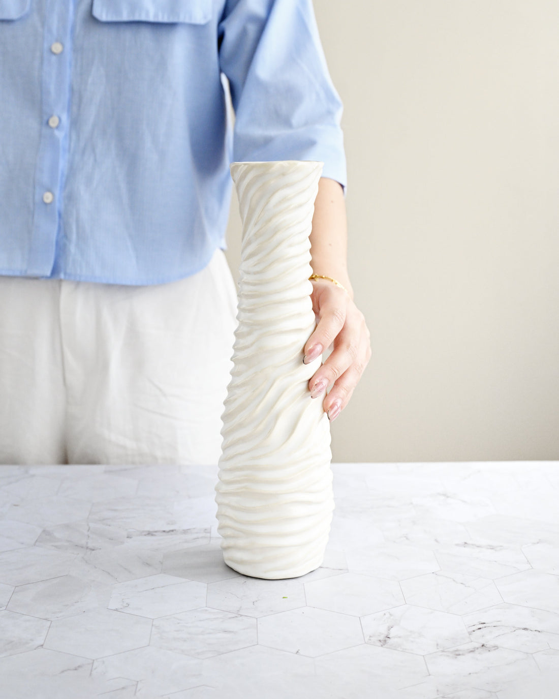 Person holding a textured white vase on a marble surface with a neutral background