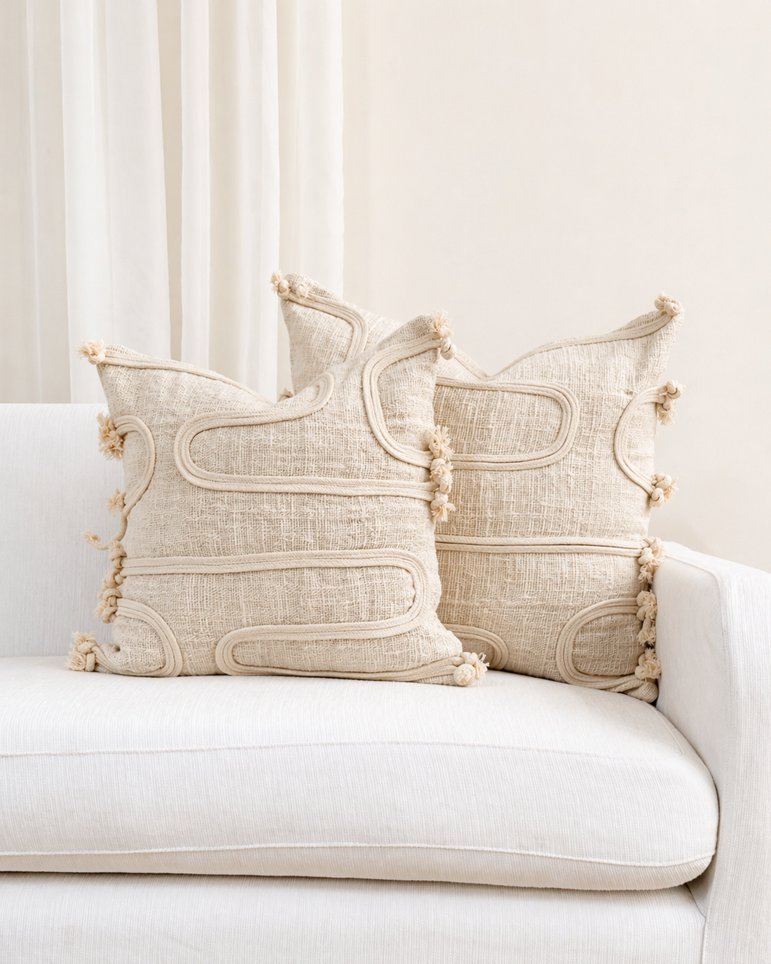 Decorative pillows with tassels on a white sofa against a neutral background