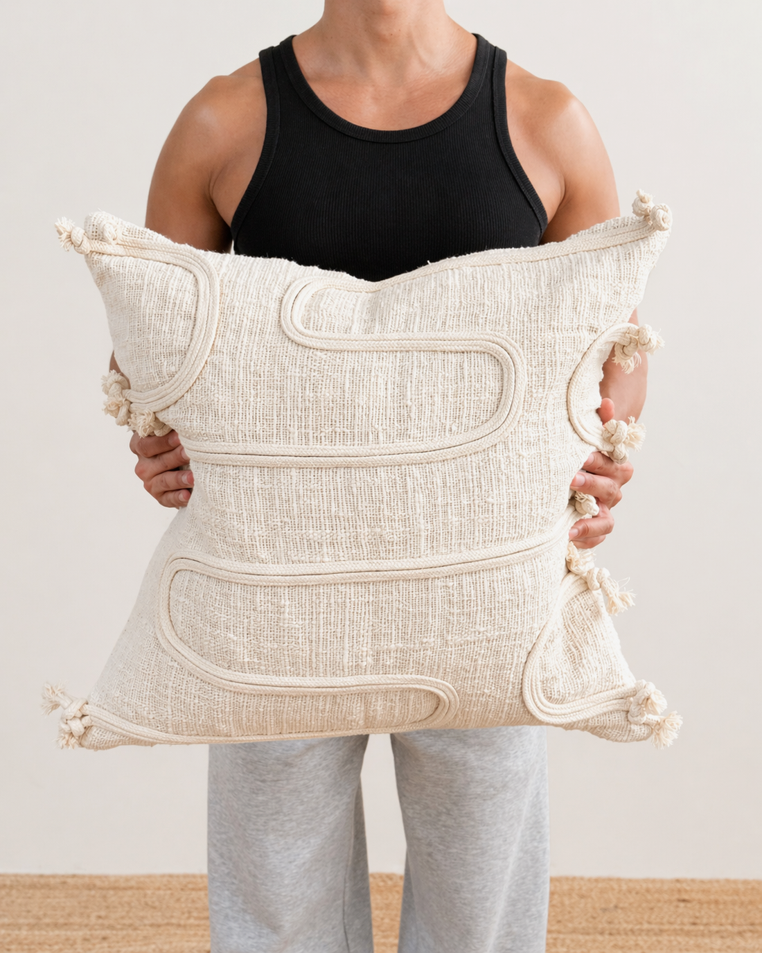 Person holding a large decorative pillow with intricate patterns and tassels.
