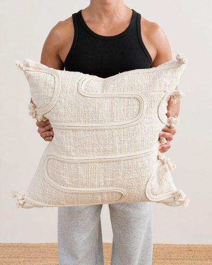 Person holding a large decorative pillow with intricate patterns and tassels.