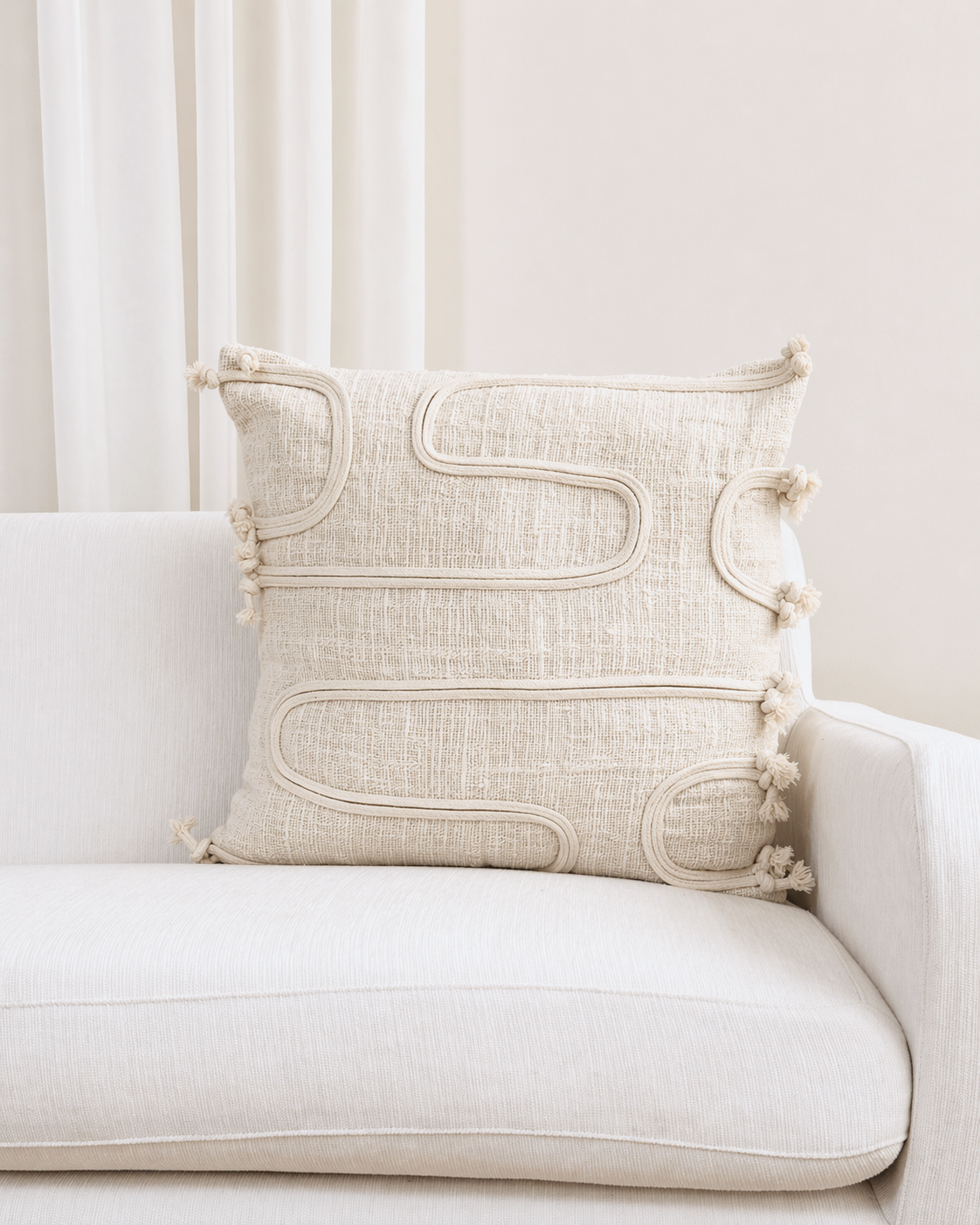 Decorative pillow with tassels on a white sofa against a white curtain background