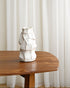 White ceramic vase on a wooden table with white curtains in the background