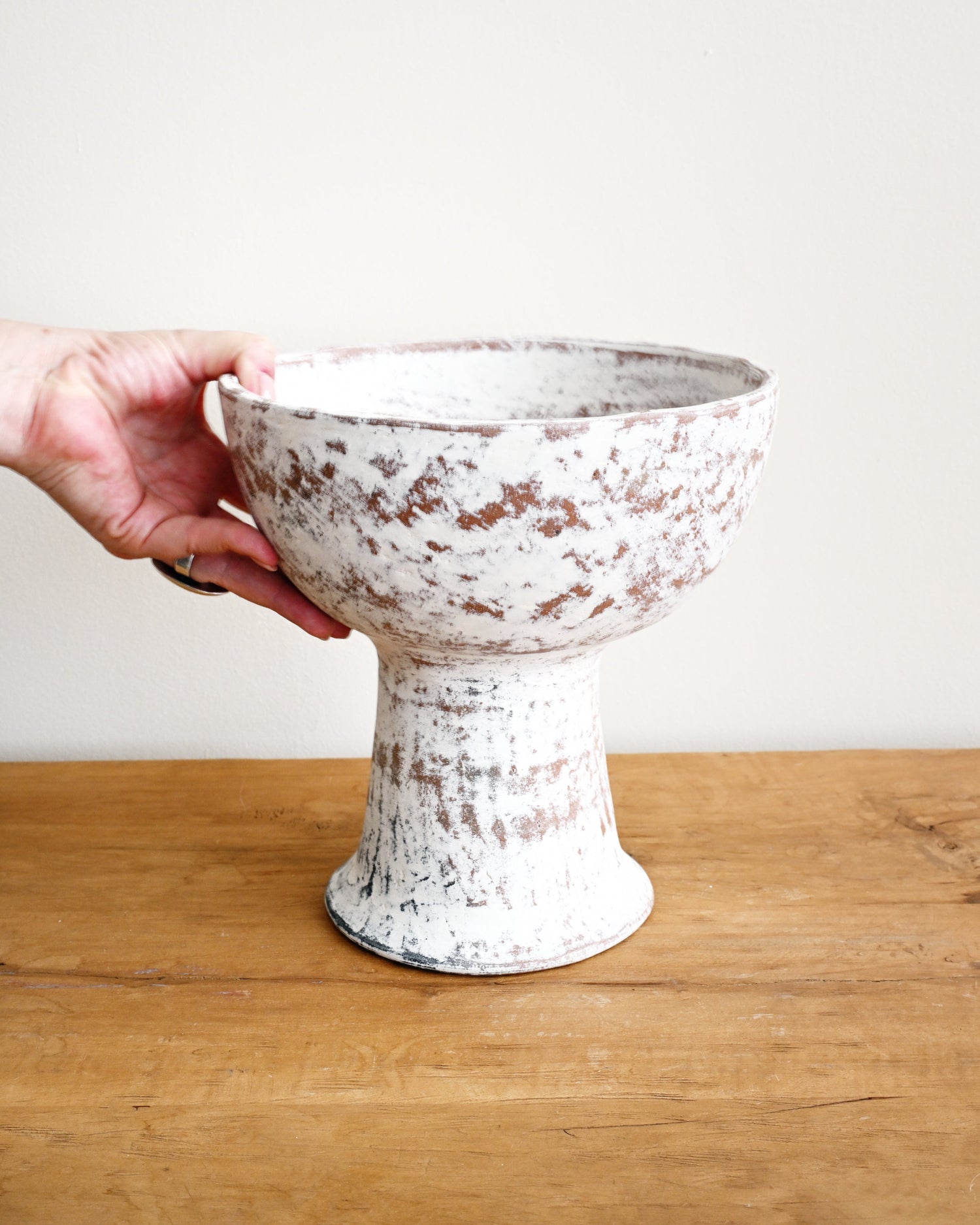 White ceramic pedestal bowl held by a hand on a wooden surface with a light background
