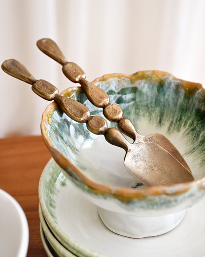 Ceramic bowl with green interior and gold spoon on a wooden surface