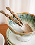 Ceramic bowl with green interior and gold spoon on a wooden surface