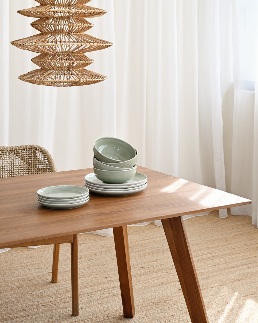 Wooden table with green ceramic bowls and a modern pendant light in a bright room.