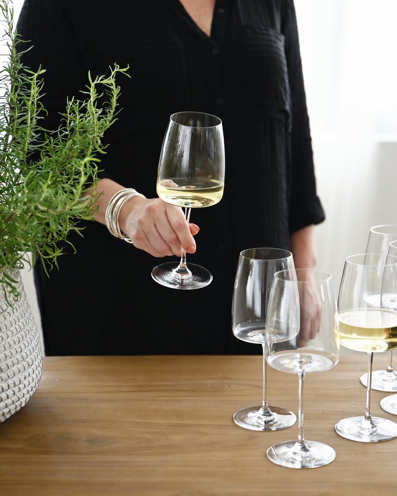 Person holding a glass of white wine with more glasses on a wooden table.