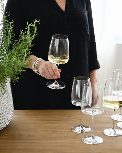 Person holding a glass of white wine with more glasses on a wooden table.