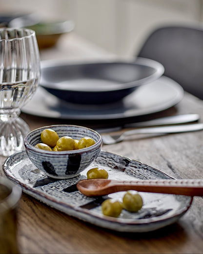 Dining table setting with ceramic bowls, plate, and small bowl on a wooden surface.