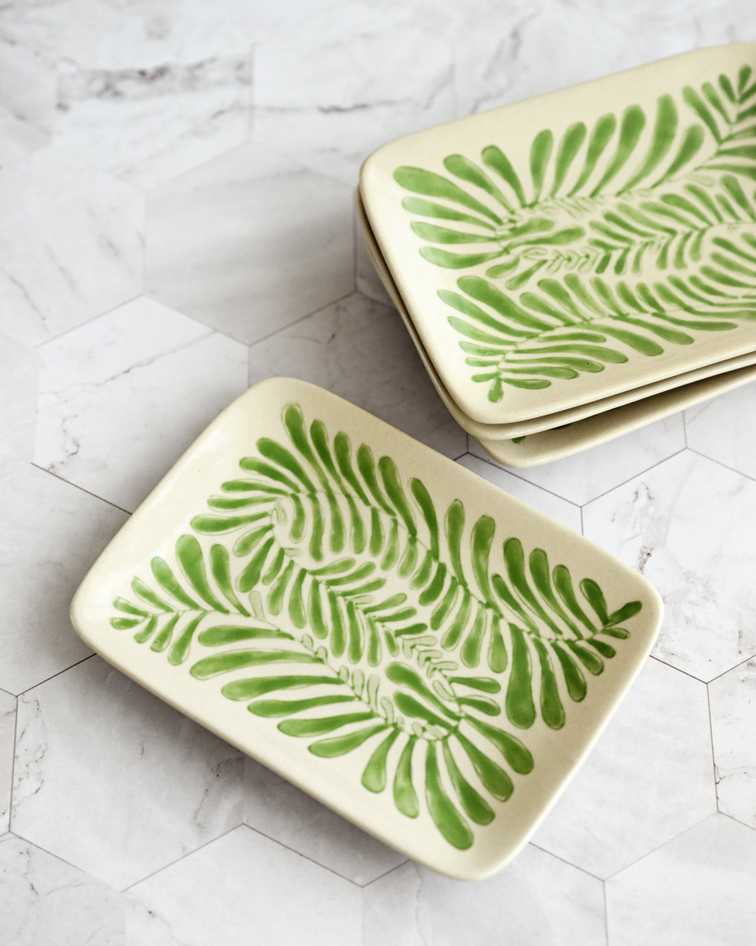 Two ceramic trays with green leaf patterns on a white marble surface