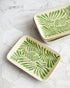 Two ceramic trays with green leaf patterns on a white marble surface