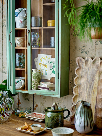 Kitchen scene with open cabinet displaying dishes, a juicer on the counter, and decorative elements.