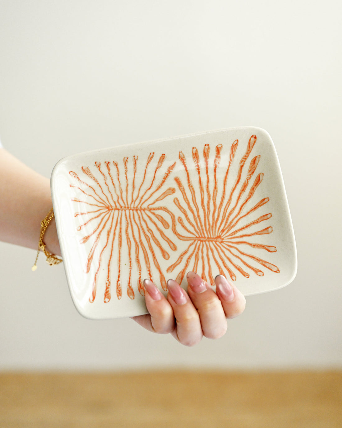 Hand holding a white ceramic tray with orange sunburst pattern against a plain background