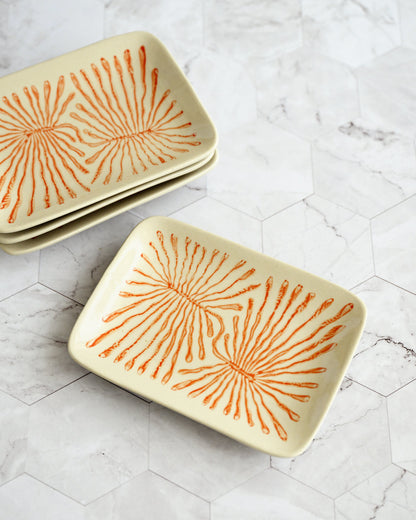 Set of ceramic trays with orange sunburst pattern on a marble surface