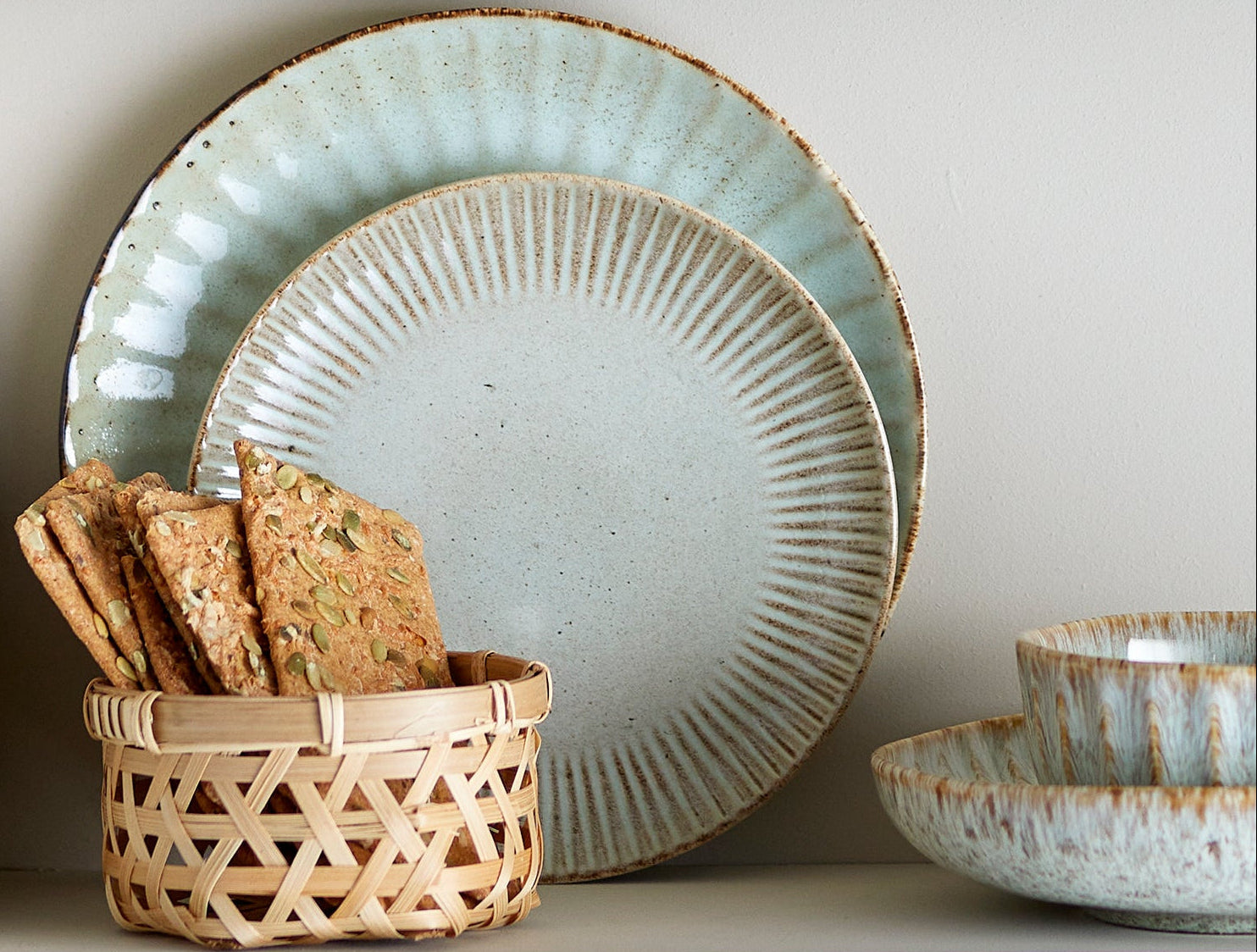 Set of ceramic plates and bowls with a basket of crackers on a white surface