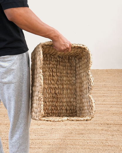 Person holding a woven basket on a wooden floor.