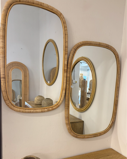 Three wall mirrors with rattan frames on a white wall above a wooden console table.