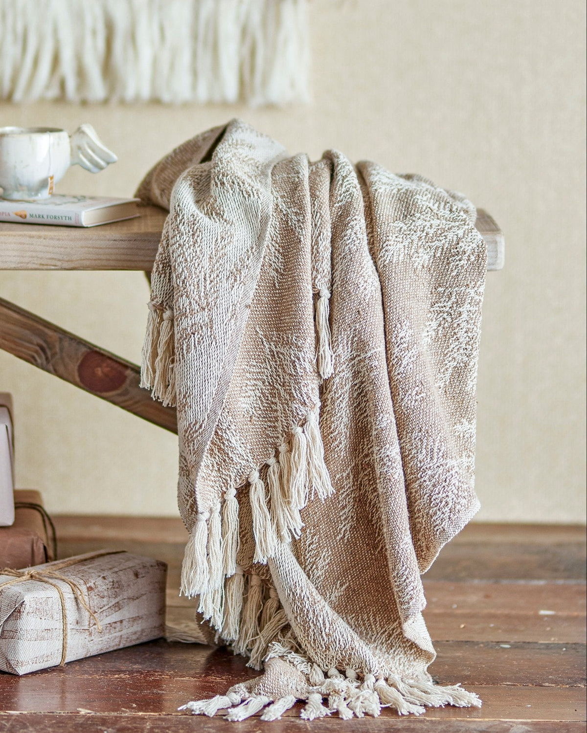 A beige and brown plaid Gabriela Throw by Bloomingville draped over the edge of a wooden table, with a cozy, festive atmosphere.