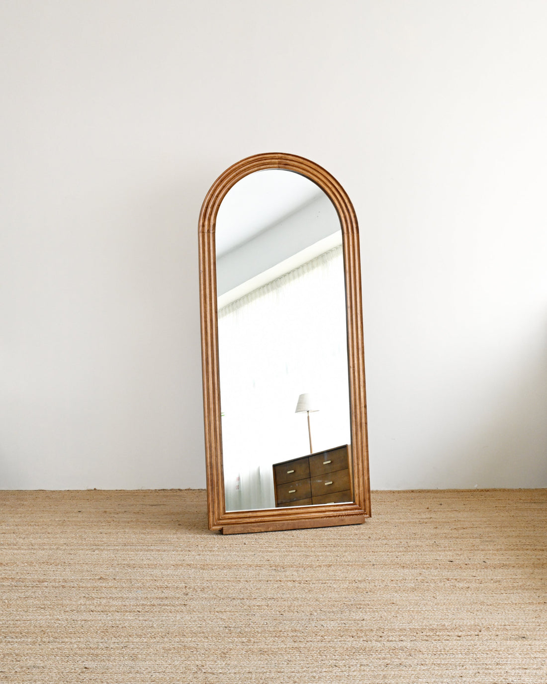 Wooden floor mirror leaning against a white wall on a wooden floor.