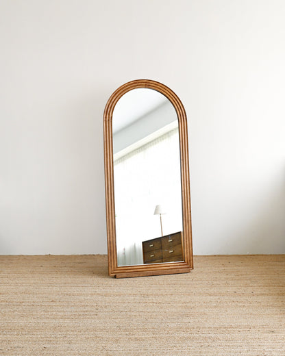 Wooden floor mirror leaning against a white wall on a wooden floor.