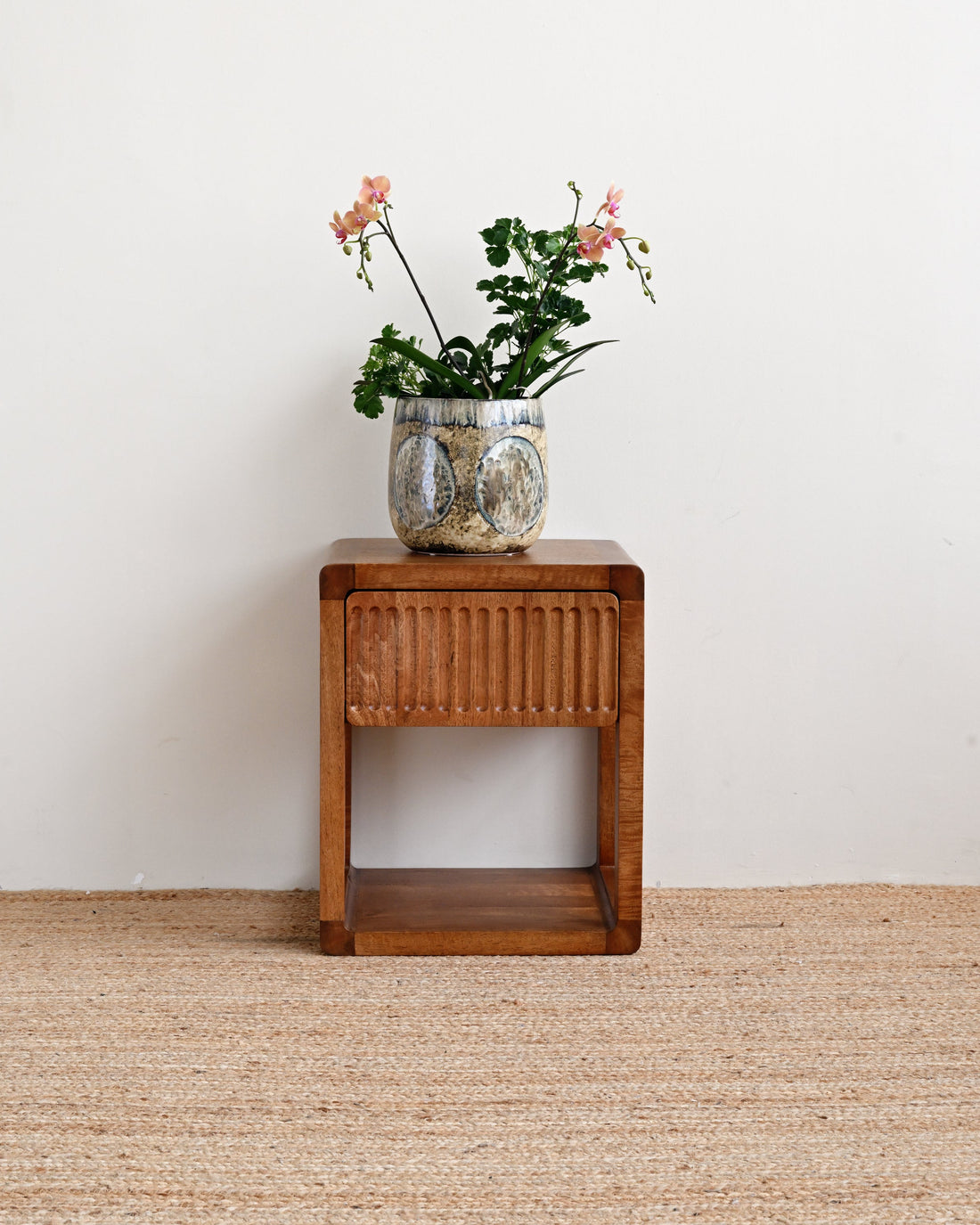 Wooden side table with a vase of flowers on a beige carpet