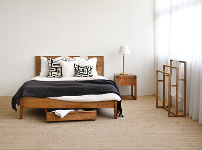 Wooden bed with storage drawers in a minimalistic bedroom setting.