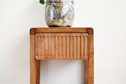 Wooden side table with a textured surface and a decorative jar on top against a white background